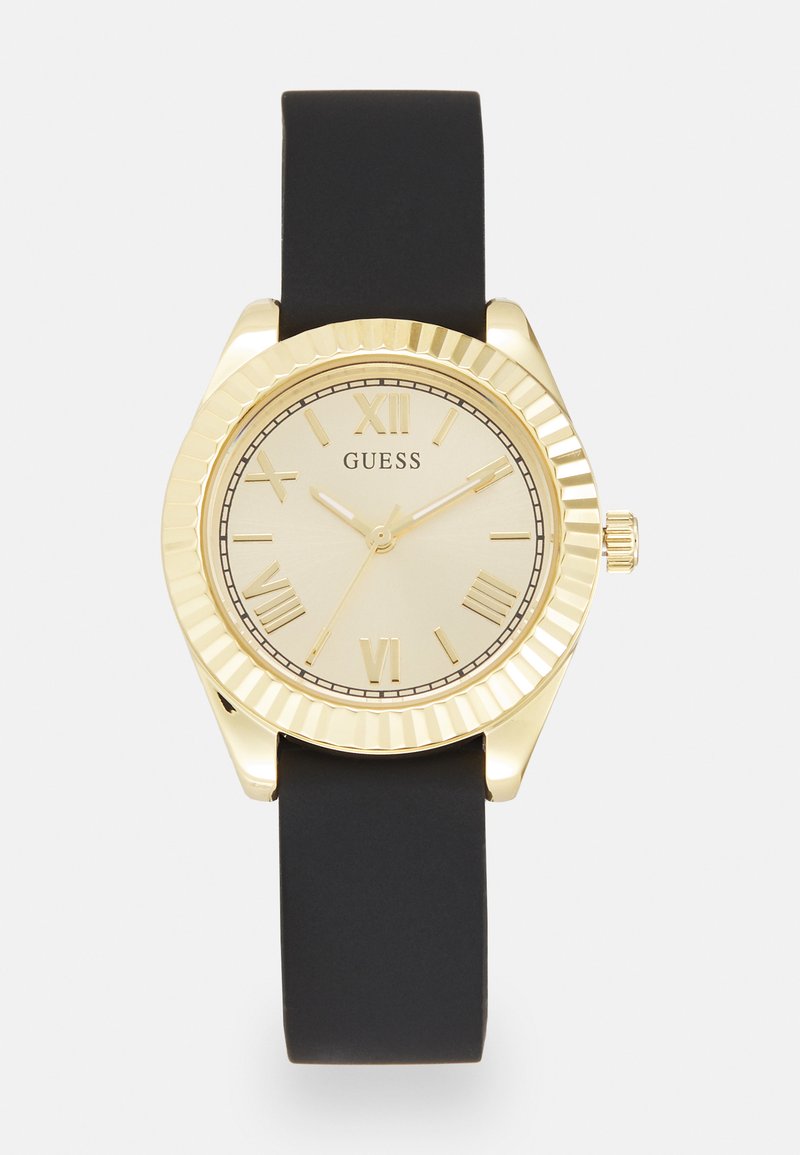 Reloj de tono dorado con una esfera redonda, correa de goma negra, números romanos y un bisel texturizado. Presenta un diseño minimalista con una esfera sencilla.