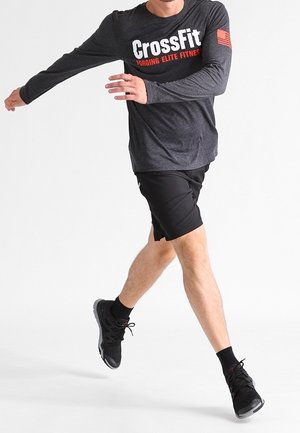 Graues Sportshirt mit langen Ärmeln und "CrossFit"-Logo, kombiniert mit schwarzen Shorts und schwarzen Sneakern, in einer dynamischen Laufpose.