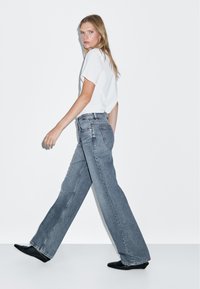 Helles blaue, weit geschnittene Jeans mit einem leicht verwaschenen Finish, kombiniert mit einem weißen Kurzarmhemd und schwarzen spitzen Ballerinas.