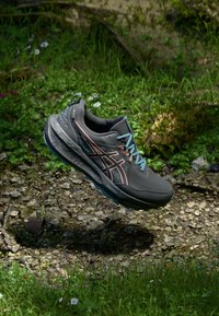 Herren Laufschuh, dunkelgrau mit Mesh-Obermaterial, blauen Schnürsenkeln und orangen Akzenten. Strukturiertete Sohle geeignet für unterschiedliches Terrain.