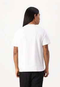 T-shirt en coton blanc avec un col rond et des manches courtes, présentant une coupe décontractée. Le dos montre un tissu lisse sans motifs visibles.