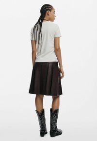 Svetlosivý bavlnený tričko, tmavá skladaná kožená sukňa, čierne vyšívané kovbojské topánky. Objekt zobrazený zozadu.