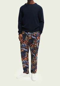 Marineblauwe trui met ronde hals, gecombineerd met gestreepte broek met kleurrijke abstracte ontwerpen, gedragen met witte sneakers.