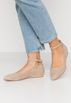 Beżowe zamszowe baleriny z końcem w szpic i paskiem na kostce, płaską podeszwą oraz lekko wygiętym tyłem. Noszone z jasnoniebieskimi dżinsami z podwiniętymi nogawkami.