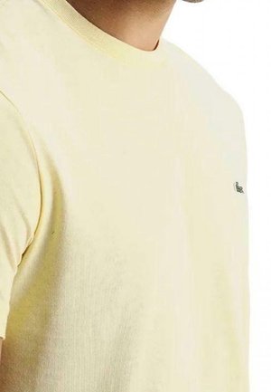 Helles gelbes Baumwoll-T-Shirt mit Rundhalsausschnitt, kurzen Ärmeln und einem kleinen grünen Logo auf der linken Brust. Geschmeidige Textur und klassischer Schnitt.