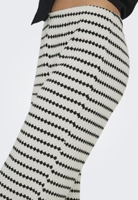 Leggings a righe bianche e nere con design a zigzag. Il tessuto sembra testurizzato, presenta una vita elastica e tasche laterali.