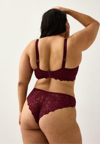 Burgundy spetsbehå och matchande trosor med delikata blommönster, justerbara band och vågiga kanter vid midjan och benöppningarna.