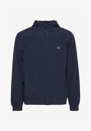 Námořnická modrá bunda s kapucí a celopropínacím zipem, elastickými manžetami a malou nášivkou na hrudi. Lehká, hladká textura.