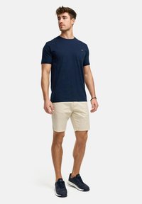 Tricou bleumarin cu mânecă scurtă, dotat cu un buzunar, asortat cu șorturi bej și adidași bleumarin. Design simplu, textură moale și stil casual.