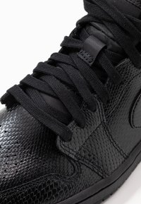 Musta teksturoitu lenkkari, jossa on matelija-inspiroitu kuvio, litteät mustat nauhat, pehmustettu kieli ja kumipohja. Minimimaalinen brändäys näkyvissä.