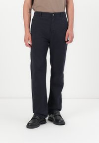 Marineblauwe katoenen broek met een rechte pijp, voorzien van een vo Closure met knoop aan de voorkant en zijzakken, gecombineerd met zwarte schoenen.