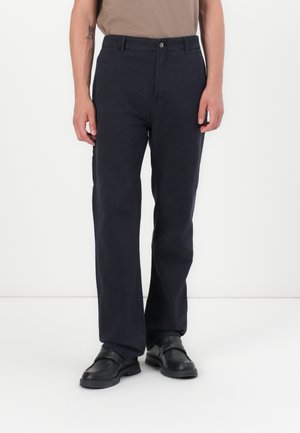 Navy cotton trousers with a straight leg, featuring a front button closure and side pockets, paired with black shoes.