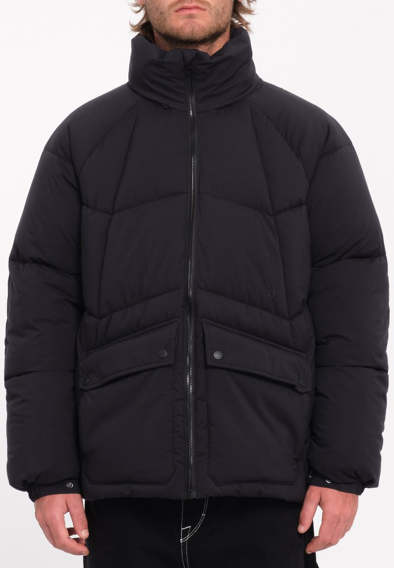 Zwarte pufferjack met een hoge kraag, geborduurd patroon, twee voorkruispockets en ritsopening. Beschikt over elastische manchetten en een iets oversized pasvorm.