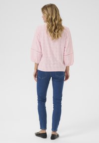 Top in cotone rosa chiaro con design ad occhielli, maniche a sbuffo a tre quarti, abbinato a jeans skinny blu e ballerine nere. Visuale posteriore mostrata.