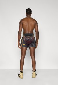 Μαύρο σατέν σορτς με κόκκινα και πορτοκαλί γραφικά σχέδια, με ελαστική μέση. Φοριέται με μπεζ υποδήματα.