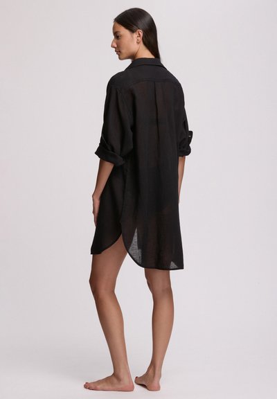 Μαύρο φόρεμα πουκάμισο από λινό με άνετη εφαρμογή, μακριά μανίκια διπλωμένα ως τους αγκώνες, πλευρικές σχισμές και ίσια στρίφωση, με κλασικό γιακά.