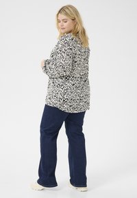 Langärmlige Bluse im schwarz-weißen abstrakten Muster, kombiniert mit dunkelblauen Jeans. Glatte Stoffqualität, lockere Passform, mit Knopfdetails.