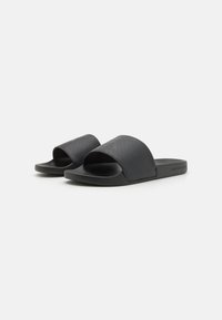 Sandales noires à glissière avec une large bande supérieure et un design ouvert sur l'avant. Fabriquées en matériau synthétique texturé avec une esthétique minimaliste.