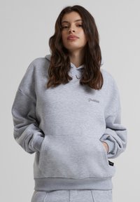 Pilkas džemperis su kapišonu, su priekinėmis kengūros kišenėmis ir gipiūrinėmis rankovėmis. Subtilus „Uždrausta“ logotipas išsiuvinėtas krūtinės srityje.