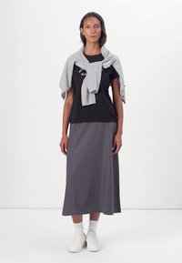 Tricou negru cu text alb, pulover gri înfășurat, fustă midi gri, adidași albi, prezentate pe un fundal alb simplu.