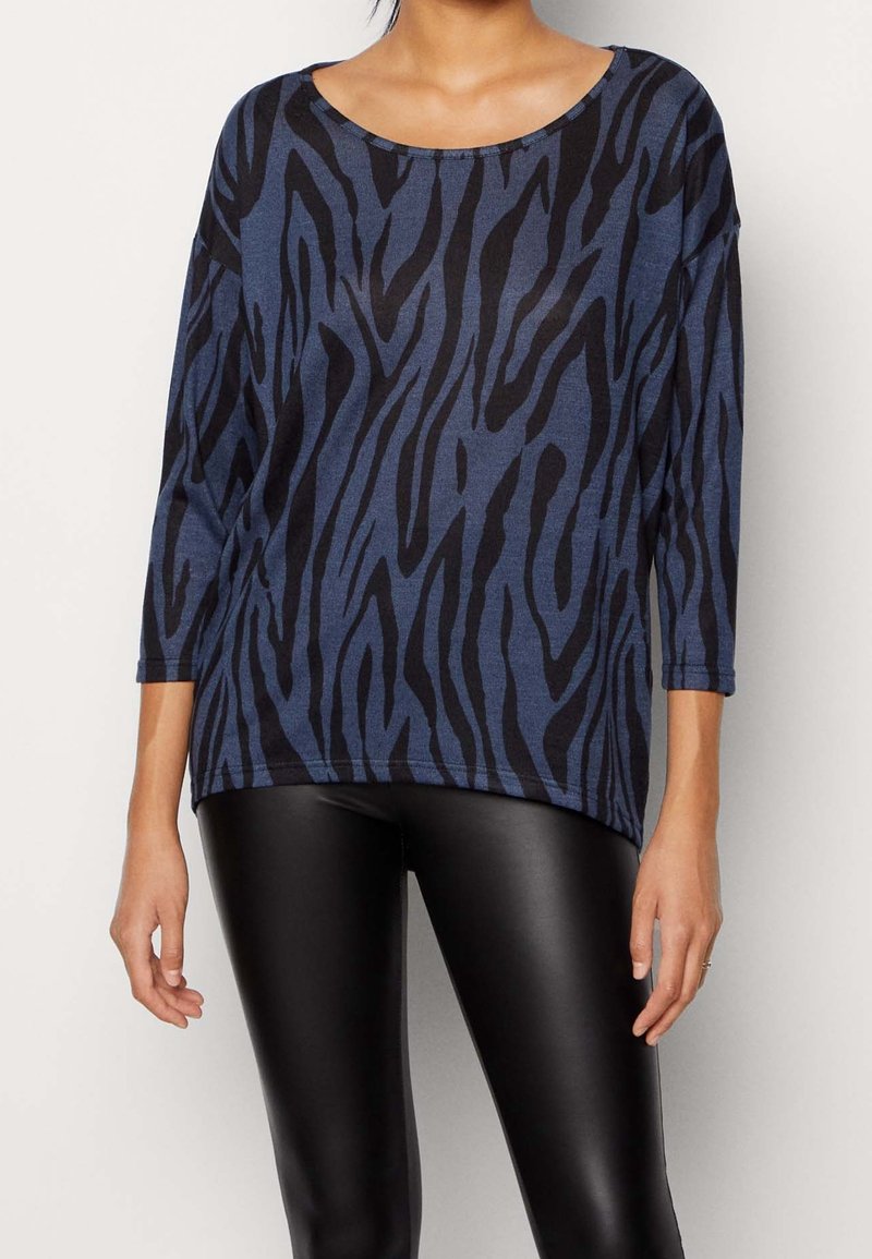 Mörkblå topp med svarta zebrarandningar, med en bred ringning och 3/4 ärmar, tillverkad av mjukt, strukturerat tyg. Kombinerad med svarta leggings.