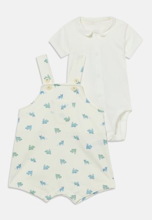 Kreemjas beebipükskostüüm dinosauruse mustriga ja sobiva lühikeste varrukatega valge kehasärgi, millel on nööbitav esikülg ja Peter Pani krae.