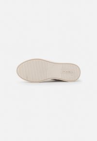 Cream-colored rubber shoe sole with horizontal ridges and a textured design. Features a discreet logo embossed on the heel area.