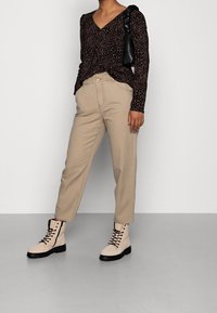 Pantalones de tiro alto color beige con un ajuste relajado, combinados con una blusa negra de manga larga con un estampado de leopardo y botas de tobillo color beige con cordones.