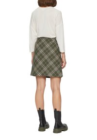 Zielona spódnica w kratę z dopasowaną talią, w kształcie litery A i gładką teksturą; zestawiona z białą bluzką z długim rękawem i czarnymi botkami za kostkę.