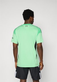 Svetlozelené športové tričko s krátkymi rukávmi, čiernymi bočnými panelmi, okrúhlym výstrihom a logom na ľavom rukáve; hladká textúra.