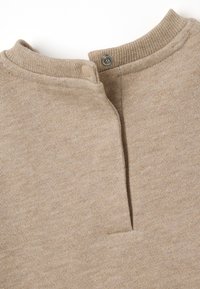 Top in maglina beige con colletto alto, dotato di chiusura a pressione e un sottile motivo testurizzato. Tessuto liscio con una finitura morbida.