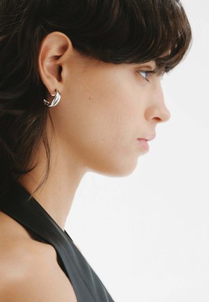 Pendientes de plata con un diseño curvado, que presentan una superficie lisa y reflectante. Llevados en el lóbulo inferior, complementan una apariencia elegante.