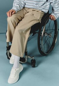 Beige vida byxor med sidofickor och en blårandig långärmad topp. Skorna består av vita sneakers och ribbade strumpor.