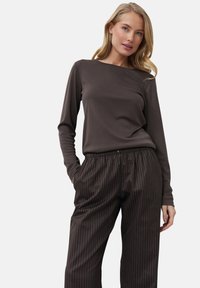 Braunes Langarmoberteil mit Rundhalsausschnitt, kombiniert mit braunen gestreiften weitgeschnittenen Hosen, die einen elastischen Bund und seitliche Taschen haben.