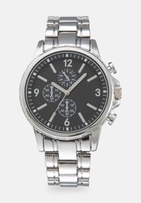 Montre chronographe en acier inoxydable argenté avec un cadran noir, présentant des index horaires blancs, trois sous-cadrans et un bracelet à maillons texturé.