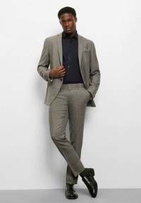 Grauer karierten Anzug mit maßgeschneiderter Passform, kombiniert mit einem dunkelblauen Hemd und Einstecktuch. Schwarze elegante Schuhe runden das Outfit ab.