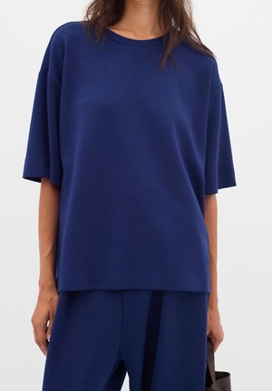 Navy blue oversized t-shirt, short sleeves, round neckline, smooth texture, featuring minimal stitching details and a relaxed fit.