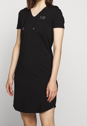 Femme portant une courte robe noire à capuche avec manches courtes et logo "EA7 Emporio Armani" sur la poitrine.