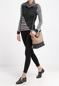 Pull en tricot avec un col bénitier noir, gris et beige ; associé à un legging noir et des chaussures plates noires ; portant un sac à main bicolore.