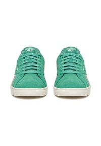 Para zielonych zamszowych trampków Reebok z białymi podeszwami, widzianych z przodu, pokazujących sznurowadła oraz logo na języku i boku.