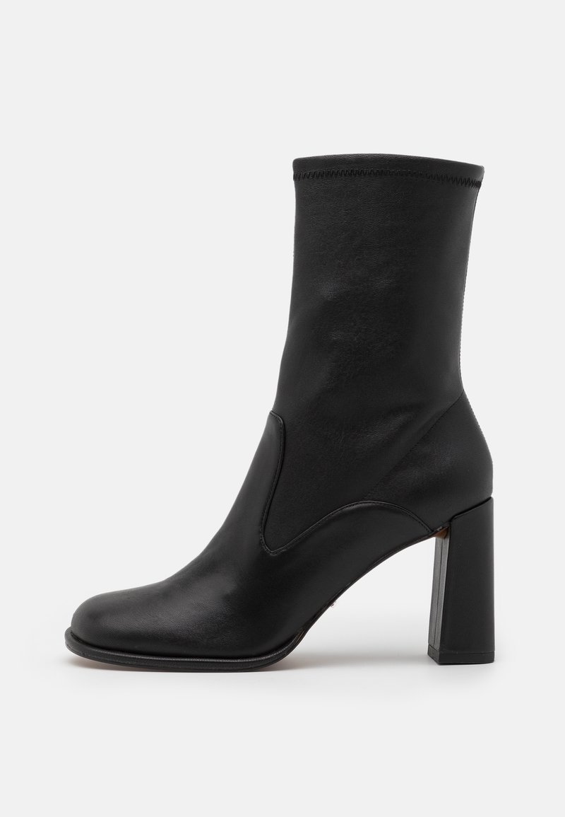 Botte noire en cuir montant jusqu'au milieu du mollet, avec un bout arrondi et un talon bloc épais, texture lisse et couture simple le long du bord supérieur.