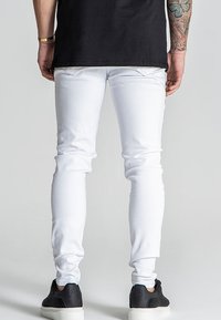 Valkoiset slim-fit farkut, jotka on valmistettu denimmateriaalista. Farkuissa on sileä pinta, minimalistinen muotoilu ja viisi taskua, jotka on yhdistetty mustiin lenkkareihin.