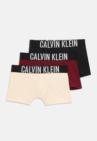 Trois paires de boxers Calvin Klein en beige, bordeaux et noir. Chacun a une large ceinture noire avec le logo blanc "CALVIN KLEIN".