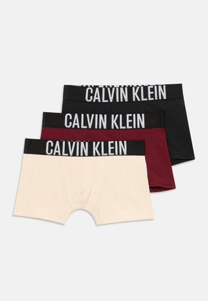 Drie paren Calvin Klein boxershorts in beige, bordeauxrood en zwart. Elk heeft een brede zwarte tailleband met de witte branding "CALVIN KLEIN".