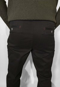 Pantaloni neri in cotone con due tasche posteriori rifinite da cuciture rosse e chiusura con bottone. Il tessuto sembra liscio e resistente.