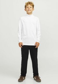 Vit långärmad turtleneck-tröja i kombination med svarta kordbyxor. Bruna sneakers med snörning och beige detaljer fulländar outfiten.