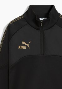 Chaqueta pullover negra con cuello alto, acentos dorados, media cremallera y un logo con la palabra "KING" en dorado en el pecho.
