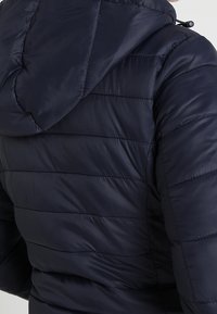 Mörkblå puffjacka med huva, quiltat mönster och en slät, blank yta. Inkluderar dragskojusteringar på huvan.