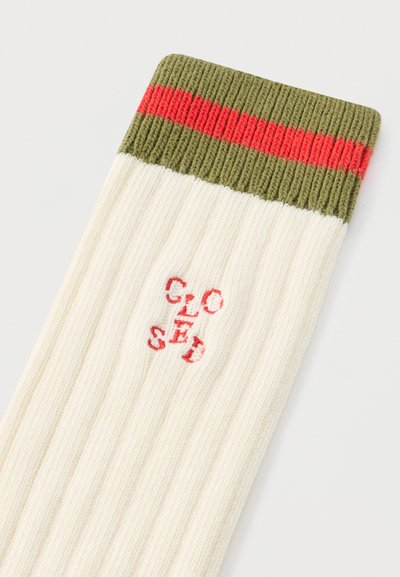 Ριμπ κάλτσες σε κρεμ χρώμα με πράσινες και κόκκινες ρίγες στο τελείωμα. Διαθέτουν κεντημένο λογότυπο "CLOSED" σε κόκκινο. Μαλακό πλεκτό υλικό με απαλή υφή.