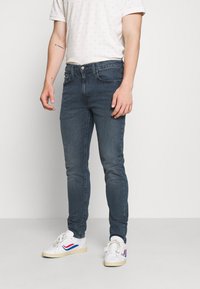 Mörkblå smala jeans i denim, med en klassisk femficksdesign och knappstängning, tillsammans med vita sneakers.